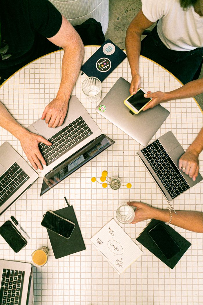 about-us-01 Top view of a team collaborating with laptops, phones, and notes in a modern office.